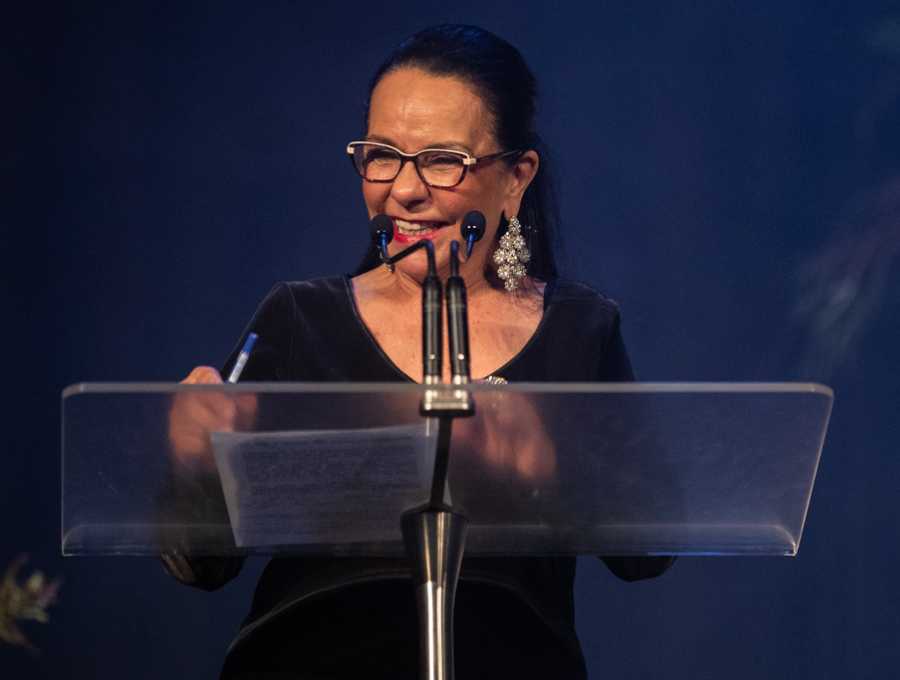 Linda Burney on stage at the 2022 Indigenous Governance Awards. She is smiling, wearing a black dress, standing behind a clear podium.