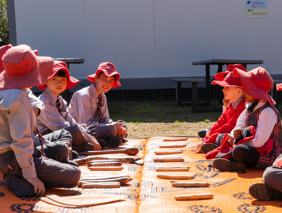 A group of schoolchildren sitting on a mat with a variety of Aboriginal tools and instruments.