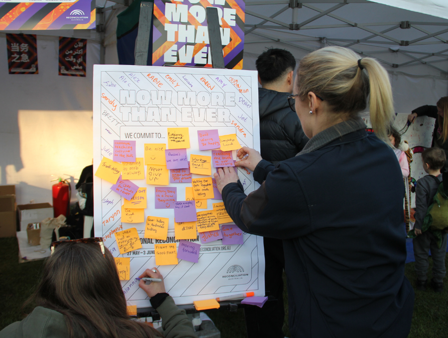 Woman with blonde hair in pony tail adds a post-it note to a board filled with purple and orange post-it notes.